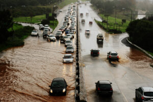 Cars drive through a flooded road wherein a city's water infrastructure has been damaged due to climate change.