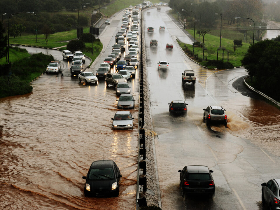 Cars drive through a flooded road wherein a city's water infrastructure has been damaged due to climate change.